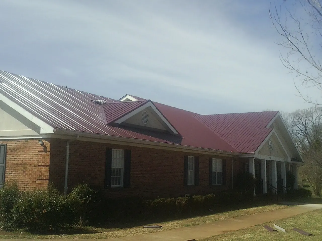 Red metal roof with gabled entries on a long brick building, from a Hail Damage Roof Repair job in Simla