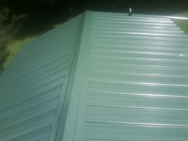 New green metal panels meeting at the ridge of a roof — Flat Roof Repair work by our crew in Simla