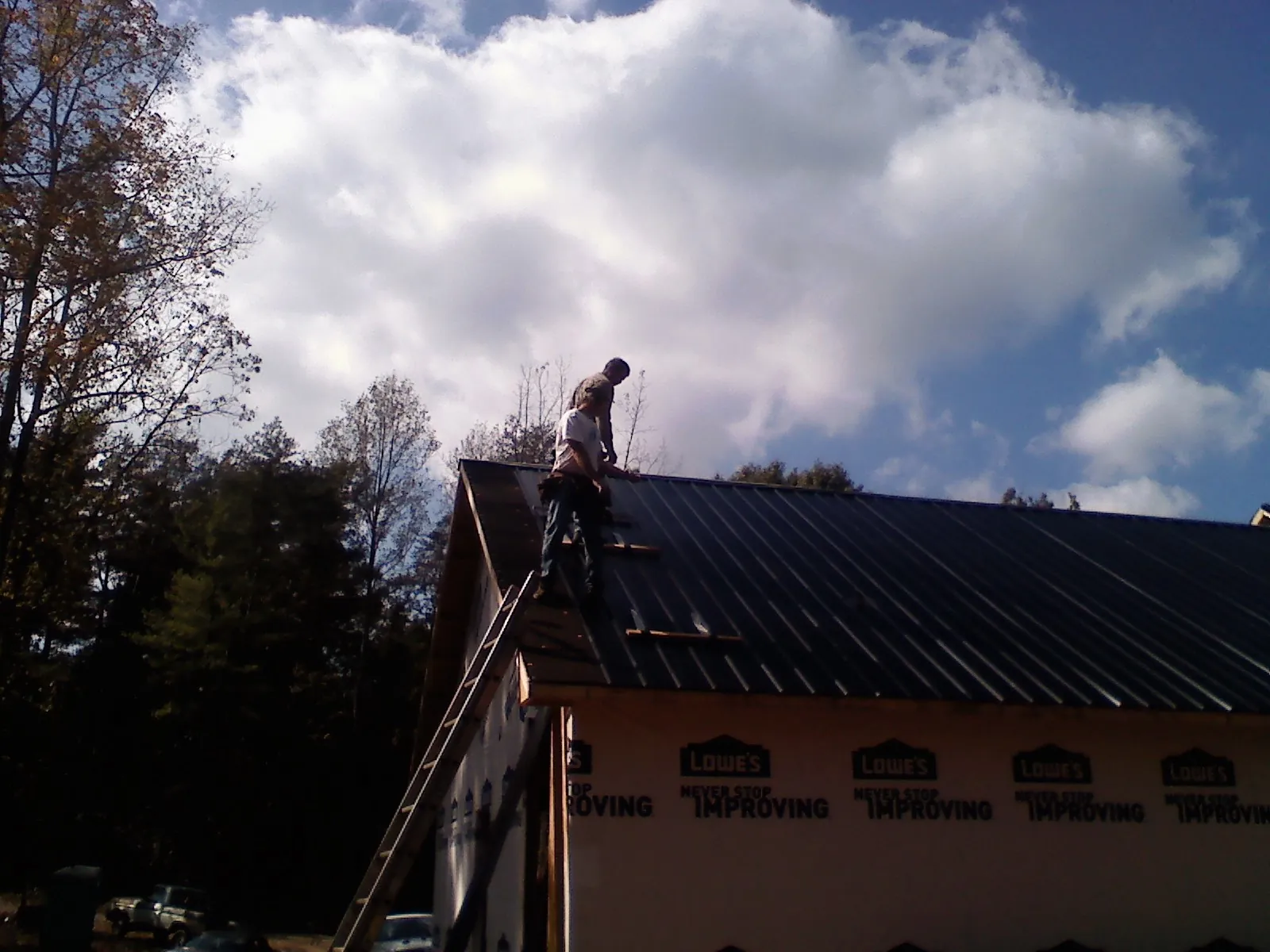 Roofer fastening dark metal panels high against a cloudy sky, from a Roof Inspection job in Simla